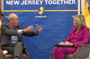 Gov. Phil Murphy sitting onstage Linda Bowden, chair of the New Jersey State Chamber of Commerce.