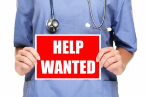 Medical professional holding a help wanted sign