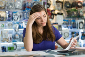 Young white woman working in computer shop, checking bills and invoices with worried expression