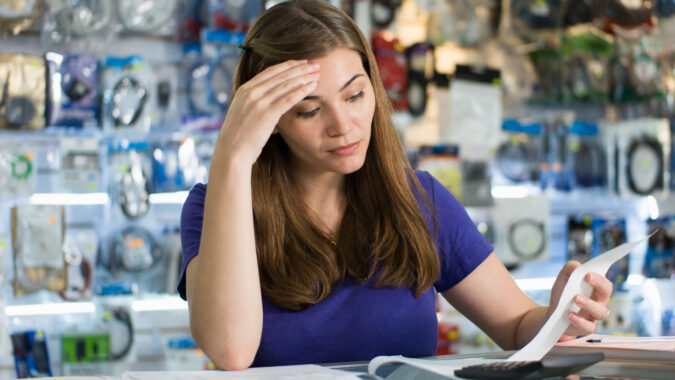 Young white woman working in computer shop, checking bills and invoices with worried expression
