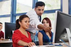 Two women at computer terminals being instructed by male