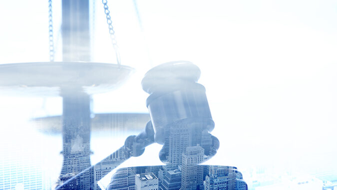 A multiple exposure of a gavel and scales of justice blended with an urban city scene.