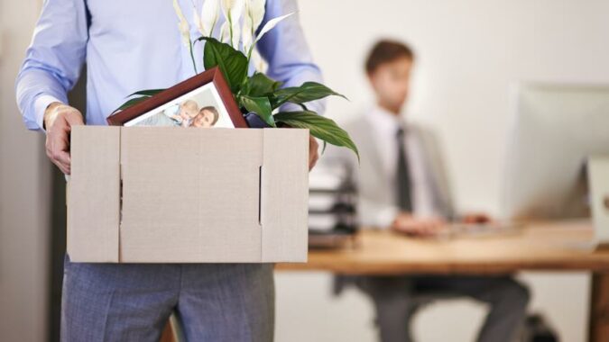 Employee carrying a box of his stuff out of the office.