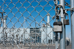 Padlock on a chain link fence with factory after layoff notices in the background