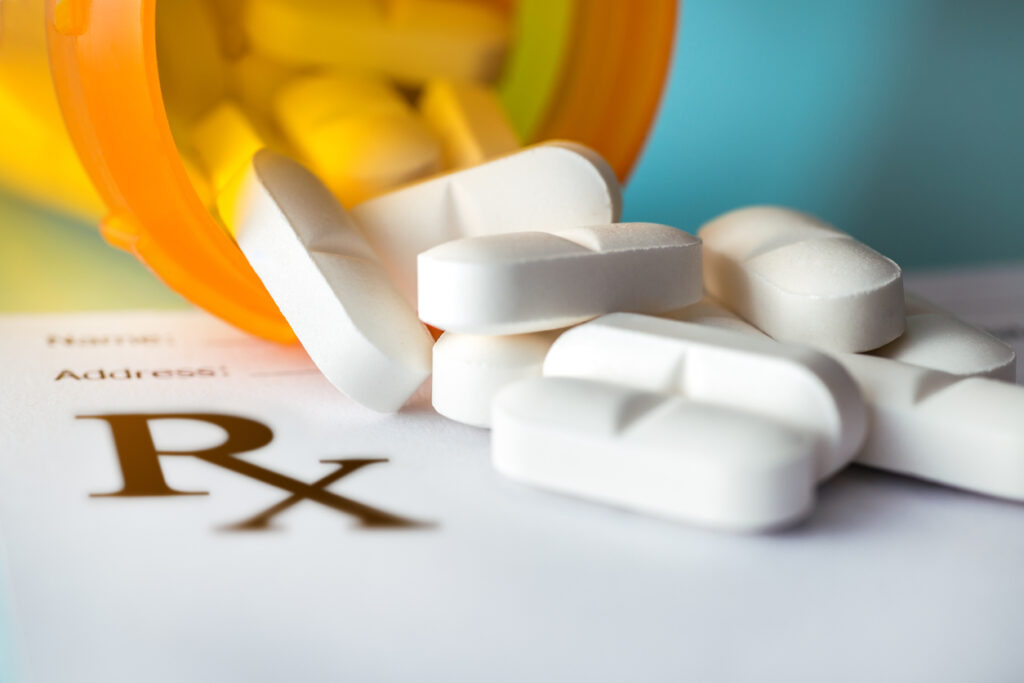 Prescription pills spilling out of a pill bottle near an Rx sign.