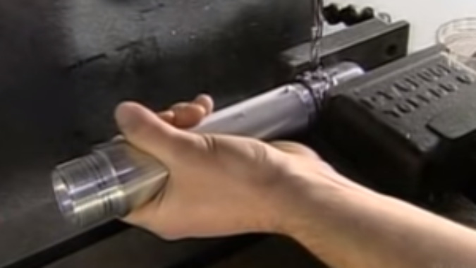 I hand holding a metal tube in a vice as part of a manufacturing process.
