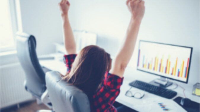 Woman sitting in front of computer with her arms raised in triumph
