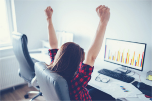 Woman sitting in front of computer with her arms raised in triumph